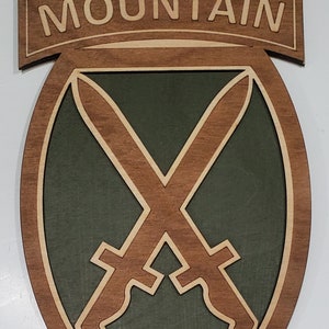 May include: A wooden plaque with the words "MOUNTAIN" in white lettering on a brown background. The plaque features a green shield with two crossed swords in brown.