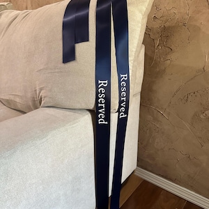 Peut inclure: Rubans de satin bleu marine avec le mot "Reserved" imprim&eacute; en blanc. Les rubans sont drap&eacute;s sur le dossier d'un canap&eacute; beige. Les rubans sont de couleur bleu fonc&eacute;.