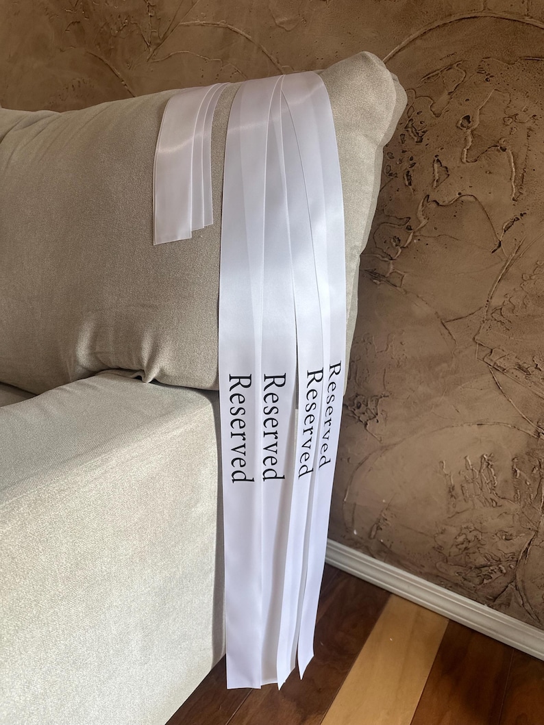 Peut inclure: Rubans de satin blancs avec le mot "Reserved" imprim&eacute; en noir. Les rubans sont drap&eacute;s sur un canap&eacute; beige. L'arri&egrave;re-plan pr&eacute;sente un mur brun textur&eacute;.
