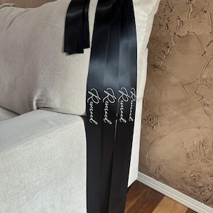 Peut inclure: Rubans de satin noirs avec le mot "Reserved" en &eacute;criture blanche &eacute;l&eacute;gante. Les rubans sont drap&eacute;s sur le bras d'un canap&eacute; beige clair. L'arri&egrave;re-plan est un mur brun textur&eacute;.