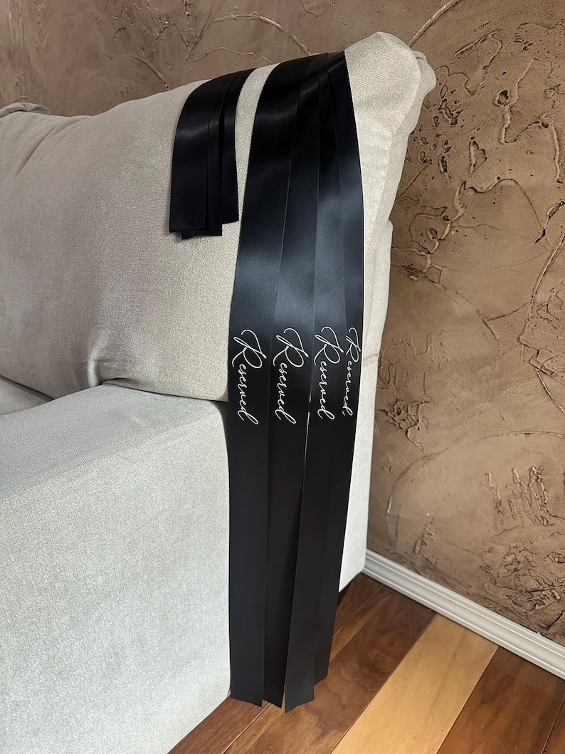 Peut inclure: Rubans de satin noirs avec le mot "Reserved" en &eacute;criture blanche &eacute;l&eacute;gante. Les rubans sont drap&eacute;s sur le bras d'un canap&eacute; beige clair. L'arri&egrave;re-plan est un mur brun textur&eacute;.