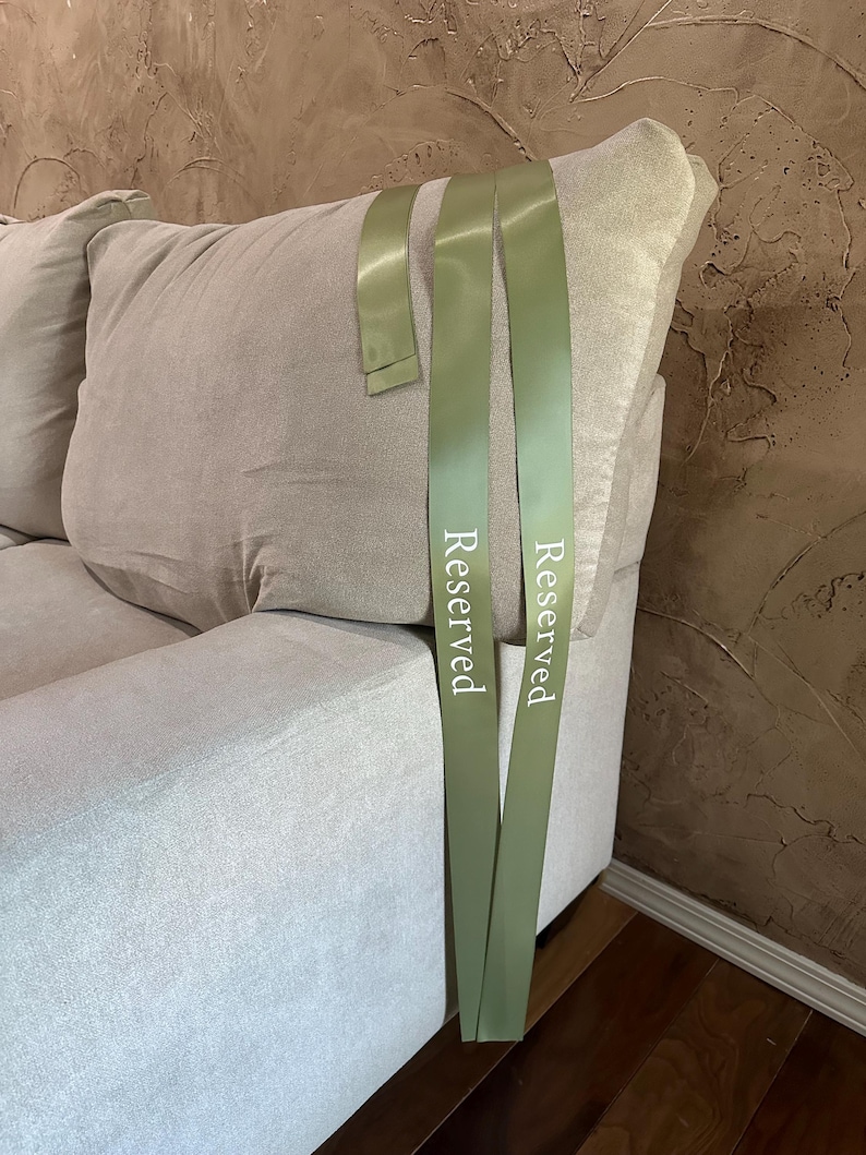 Peut inclure: Un canap&eacute; gris clair avec un grand coussin moelleux. Deux rubans vert olive avec le mot "Reserved" imprim&eacute; en blanc sont drap&eacute;s sur le canap&eacute;. L'arri&egrave;re-plan est un mur textur&eacute; et brun.