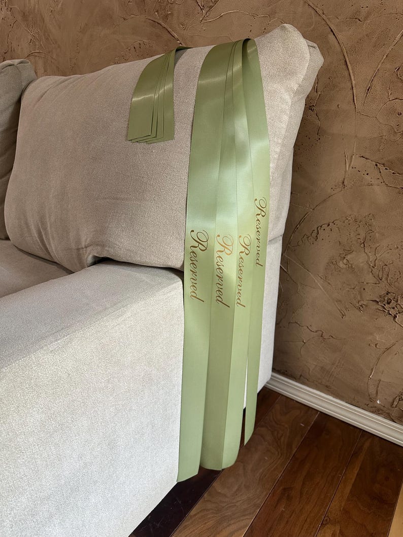 Peut inclure: Ruban de satin vert clair avec le mot "Reserved" imprim&eacute; en lettres dor&eacute;es, drap&eacute; sur le bras d'un canap&eacute; beige. Plusieurs rubans sont visibles, avec une petite pile de rubans sur le coussin du canap&eacute;.