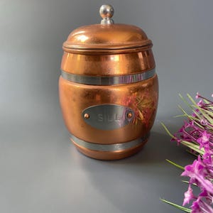 Könnte beinhalten: Kupferner Salzbehälter in Fassform mit silbernem Deckel und silbernem Etikett mit der Aufschrift "Salz".