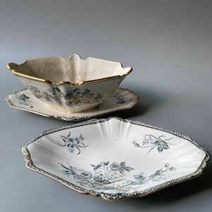 Puede incluir: Un barco de salsa de porcelana blanca con ribete dorado y un diseño floral verde. El barco está sentado en un platillo a juego.