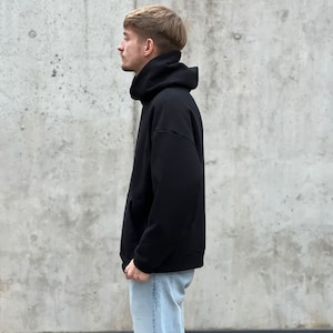 K&ouml;nnte beinhalten: Ein schwarzer Kapuzenpullover mit hohem Kragen. Der Pullover ist aus weichem, bequemem Stoff und hat eine lockere Passform.