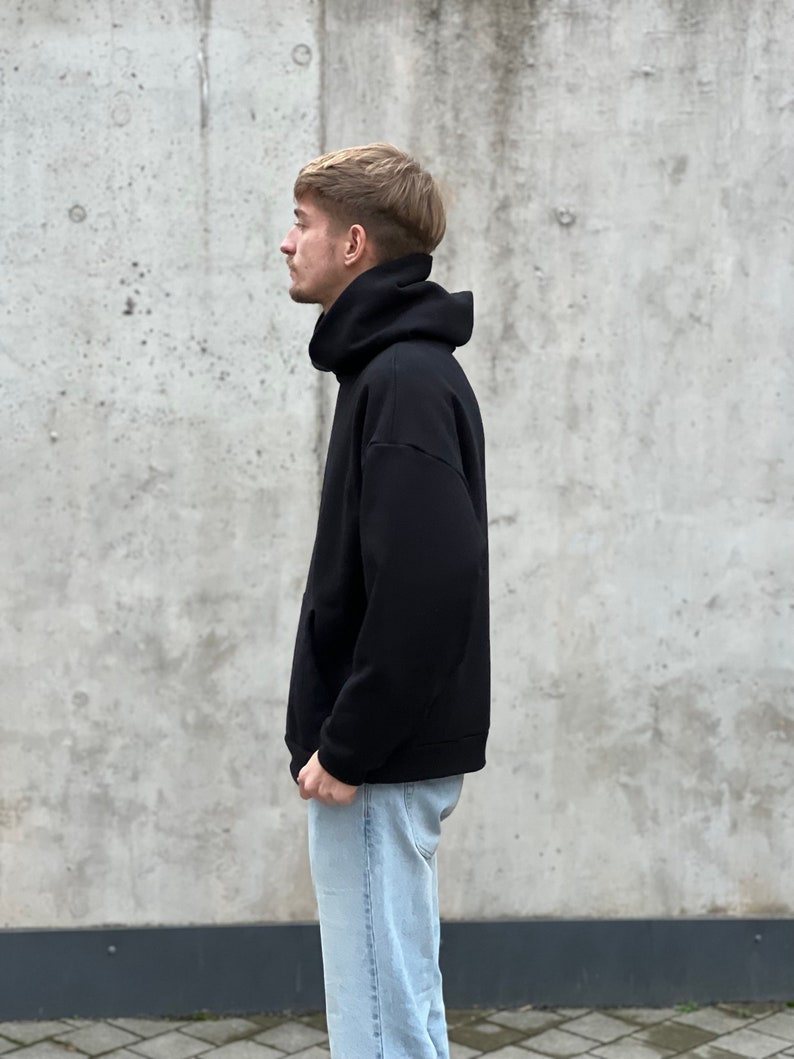 K&ouml;nnte beinhalten: Ein schwarzer Kapuzenpullover mit hohem Kragen. Der Pullover ist aus weichem, bequemem Stoff und hat eine lockere Passform.