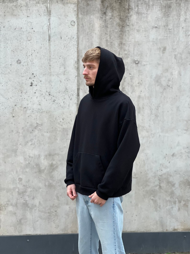 K&ouml;nnte beinhalten: Ein schwarzer Kapuzenpullover mit einer K&auml;ngurutasche. Der Pullover ist aus einem weichen, bequemen Stoff und hat eine lockere Passform.