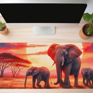 Puede incluir: Una alfombrilla de ratón colorida con una escena de puesta de sol con tres elefantes. El elefante más grande está en primer plano, con dos elefantes más pequeños detrás. La puesta de sol es de un naranja y rojo vibrantes, con un gran sol brillante en el fondo.