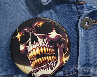 May include: A circular pinback button featuring a graphic illustration of a skull wearing dark sunglasses. The skull has prominent gold-colored teeth and is set against a dark background with bright, star-like light flares accenting the design.
