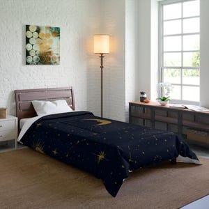 May include: A navy blue comforter featuring a celestial design with a gold crescent moon, sun, and stars. The bedding is on a wooden bed frame in a bedroom with a white brick wall and a window.