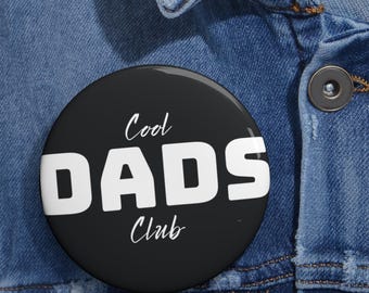 May include: A circular pinback button with a black background and white text. The text reads Cool DADS Club, with the words Cool and Club in a cursive script font and the word DADS in a large, bold, sans-serif block font across the center.