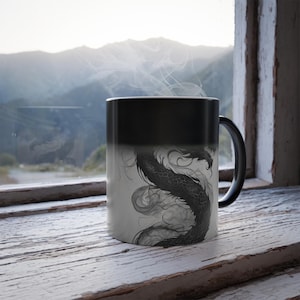 May include: A black and white heat-sensitive mug with a dragon design. The mug is black when cold and reveals the dragon design when hot.