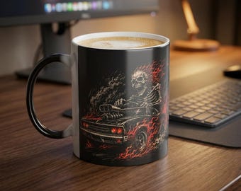 May include: A black ceramic mug featuring a graphic illustration of a skeleton driving a muscle car engulfed in bright orange and red flames. The mug has a curved handle and contains a light-colored beverage with foam visible at the top rim.