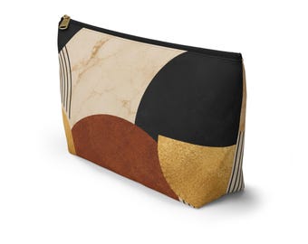 May include: A zippered pouch featuring a geometric pattern with a beige marble texture, a solid black semi-circle, a rust-colored semi-circle, and a textured gold semi-circle. The design includes thin black vertical lines on the sides and a gold zipper.