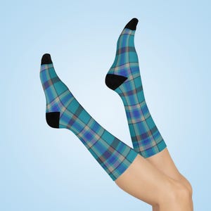 Könnte beinhalten: Kniestrümpfe mit einem türkis-, blau- und graufarbenen Karomuster. Die Socken haben schwarze Fersen und Zehen. Sie werden vor einem hellblauen Hintergrund präsentiert.