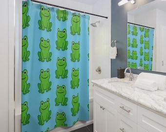 May include: A light blue shower curtain featuring a repeating pattern of bright green cartoon frogs with large eyes and smiling mouths. The frogs are arranged in a grid-like layout across the fabric, which hangs from a black metal rod.