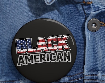 May include: A black round button with the words "BLACK AMERICAN" in white, with the word "BLACK" filled with a distressed American flag design. The button is set against a blue denim background.