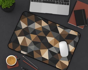 May include: A rectangular desk mat featuring a geometric pattern of triangles in shades of black, dark gray, light gray, and tan. The mat has a black border and is positioned on a dark surface alongside a laptop, a white computer mouse, notebooks, pens, and a cup of coffee.