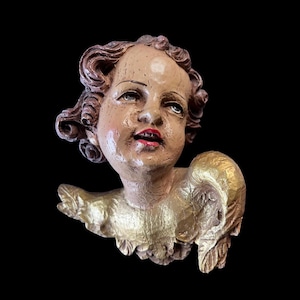 Könnte beinhalten: Vintage Cherub-Skulptur mit ruhigem Ausdruck, heller Haut, roten Lippen und lockigem braunem Haar. Die Flügel und der Kragen des Cherubs sind mit Blattgold verziert, vor schwarzem Hintergrund.