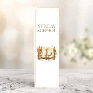 May include: A white bookmark featuring the text "SUNDAY SCHOOL" in gold. An illustration of an open book with wheat surrounds the text. The bookmark has a gold border and is on a marble surface.