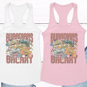 May include: Two white and pink tank tops with a retro design featuring the text "Guardians of the Galaxy" with cassette tapes, planets, and stars.