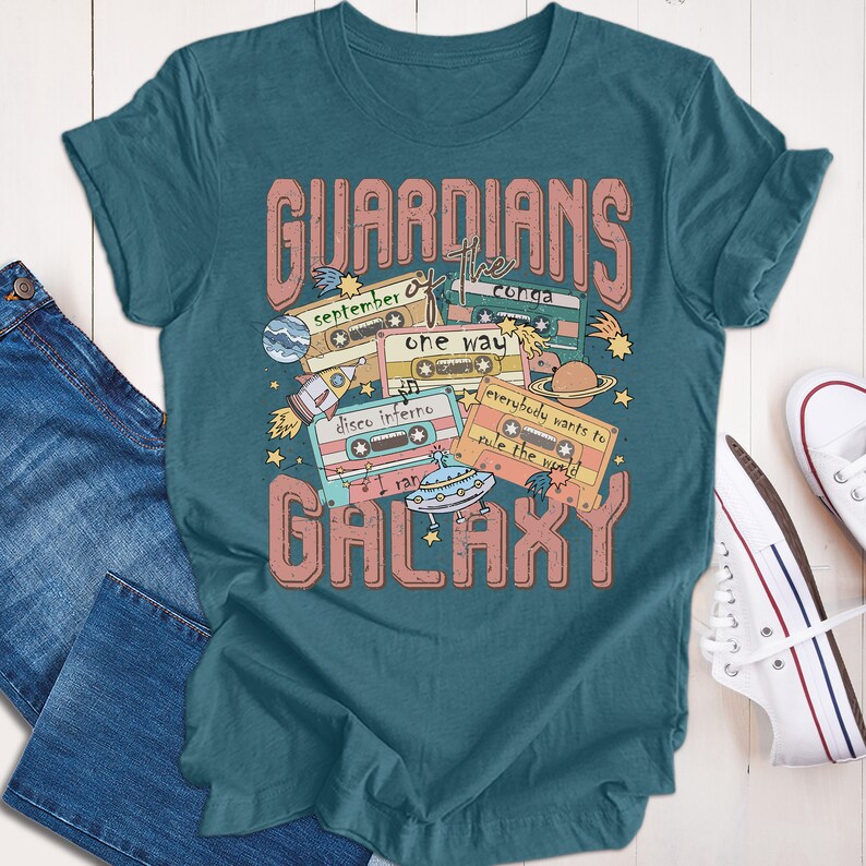 Op de afbeelding: Tealblauwe T-shirt met een grafische print van cassettebandjes en de tekst "Guardians of the Galaxy". De cassettebandjes hebben songtitels zoals "September", "Conga", "One Way", "Disco Inferno", "I Ran" en "Everybody Wants to Rule the World".