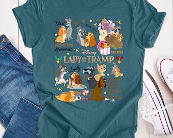 Puede incluir: Camiseta de color verde azulado con un gráfico de los personajes de La Dama y el Vagabundo de Disney, incluyendo a Dama, Vagabundo y otros perros. La camiseta tiene el texto "Start Building Some Memories" y "Disney Lady and the Tramp Est. 1955".