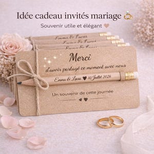 May include: A stack of beige wedding favor cards tied with twine, each featuring a pencil. The cards have the text "Merci" and "Emma & Lucas 10 Juillet 2026". Two gold wedding rings are in the foreground.