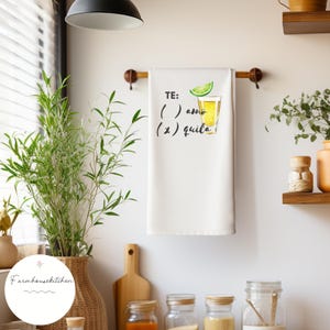 May include: White kitchen towel with the text "TE: ( ) amo (x) quila" and a watercolour illustration of a shot glass with a lime wedge and tequila.