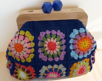 May include: A blue crocheted clutch bag with a wooden frame and blue plastic clasps. The bag is decorated with colorful crocheted flowers.