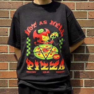 Könnte beinhalten: Ein schwarzes Kurzarm-T-Shirt mit einer Grafik eines roten Teufels, der ein Stück Pizza hält. Der Text lautet Hot As Hell Pizza, Delivery, Die-In, Takeout und $6.66. Das Design enthält grüne karierte Ränder und stilisierte Flammen.
