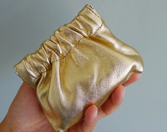 May include: A gold leather pouch with a gathered top. The pouch is soft and has a smooth, shiny finish.