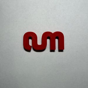 May include: A bright red, three-dimensional plastic object shaped like the lowercase letters 'nm' connected together. The piece features a smooth, solid surface with rounded edges and a uniform thickness, displaying a distinct, continuous curved form.