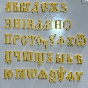 Könnte beinhalten: Eine Sammlung gelber, dreidimensionaler Buchstaben des kyrillischen Alphabets. Die Buchstaben sind in Reihen angeordnet und zeigen das gesamte Alphabet. Die Buchstaben haben eine strukturierte Oberfläche und bestehen wahrscheinlich aus einem festen Material.
