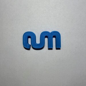 May include: A blue 3D printed plastic object shaped like the lowercase letters 'rm' connected together. The surface of the blue plastic shows a fine, linear texture consistent with additive manufacturing processes, forming a continuous shape.
