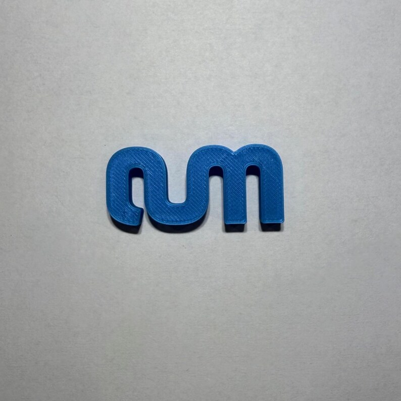 May include: A blue 3D printed plastic object shaped like the lowercase letters 'rm' connected together. The surface of the blue plastic shows a fine, linear texture consistent with additive manufacturing processes, forming a continuous shape.