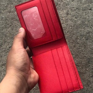 May include: A red leather wallet with a clear plastic window for an ID card. The wallet has multiple card slots and a billfold.