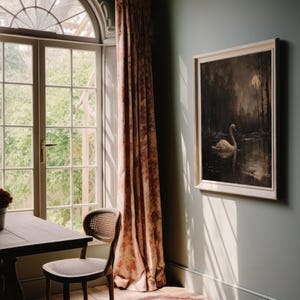 May include: A vintage-style framed print of a white swan swimming in a dark, moonlit lake. The print is hanging on a light green wall in a room with a window and a table with a chair.