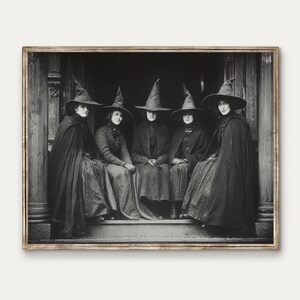 May include: A monochrome framed print shows five figures in cloaks and pointed hats, seated on steps. The vintage image has a mysterious quality, ideal for Halloween decorations. The image is reminiscent of a coven.
