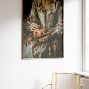 K&ouml;nnte beinhalten: Gerahmter Kunstdruck mit einem Vintage-Bild einer Person, die einen geschnitzten K&uuml;rbis h&auml;lt. Die Person tr&auml;gt ein historisches Kost&uuml;m mit wei&szlig;em Oberteil und gemustertem Rock. Der K&uuml;rbis hat ein geschnitztes Gesicht.