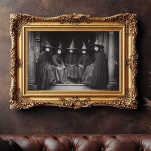 May include: A black and white photograph of six people in witch hats and cloaks, framed in an ornate gold frame. The frame is rectangular with detailed carvings. The photograph is mounted on a dark brown wall above a brown leather sofa.