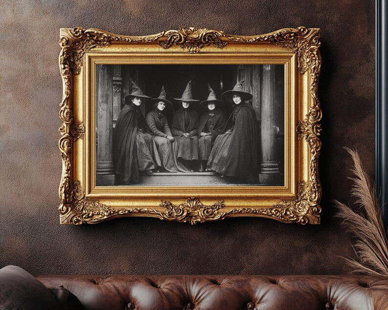 May include: A black and white photograph of six people in witch hats and cloaks, framed in an ornate gold frame. The frame is rectangular with detailed carvings. The photograph is mounted on a dark brown wall above a brown leather sofa.