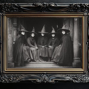 May include: A framed black and white photograph of five people in witch hats and cloaks. The ornate frame is black with gold trim. The image is set against a dark background, creating a vintage, gothic aesthetic.