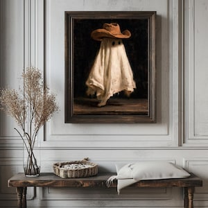 Pu&ograve; includere: Un dipinto a olio incorniciato raffigurante una figura spettrale avvolta in un lenzuolo bianco e che indossa un cappello da cowboy marrone. La figura &egrave; centrata su uno sfondo scuro, poggiata su una superficie in legno. La cornice &egrave; in legno scuro.