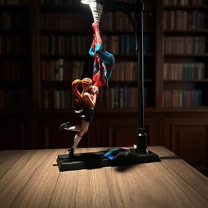 Peut inclure: Lampe d&eacute;corative repr&eacute;sentant un lampadaire noir avec une lumi&egrave;re en haut. La lampe pr&eacute;sente une figurine de Spider-Man suspendue &agrave; l'envers et une figurine f&eacute;minine en dessous. Les figurines sont rouges, bleues et noires.