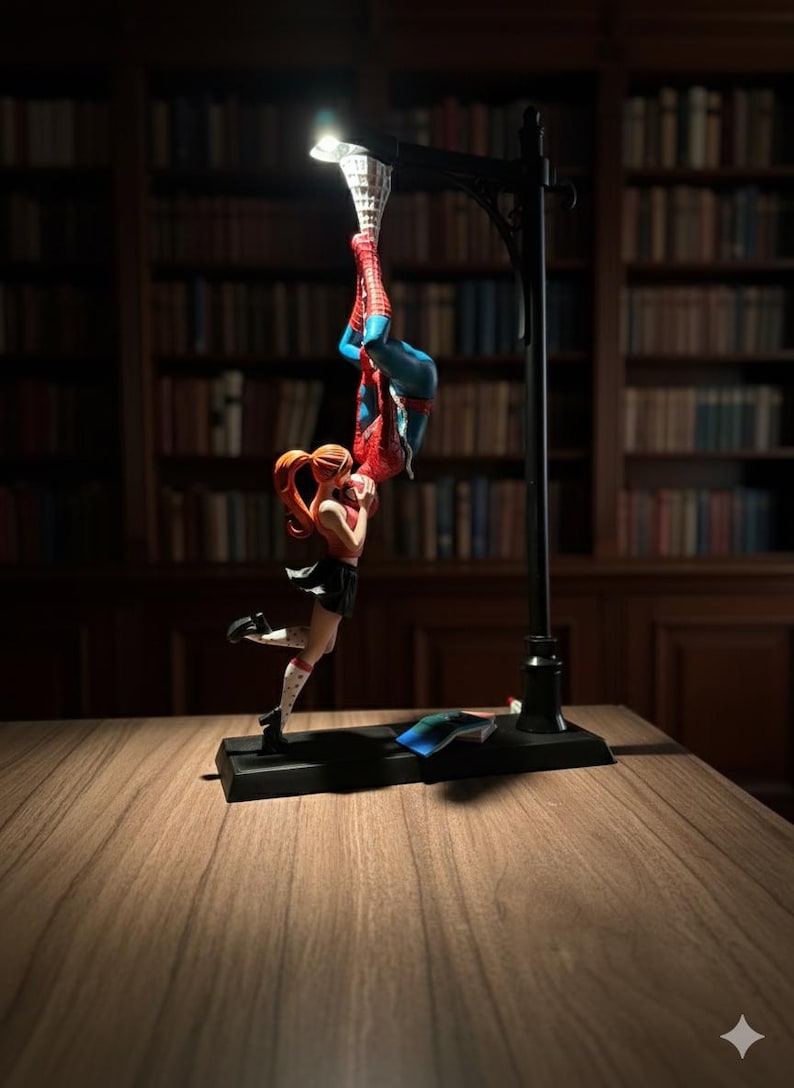 Peut inclure: Lampe d&eacute;corative repr&eacute;sentant un lampadaire noir avec une lumi&egrave;re en haut. La lampe pr&eacute;sente une figurine de Spider-Man suspendue &agrave; l'envers et une figurine f&eacute;minine en dessous. Les figurines sont rouges, bleues et noires.