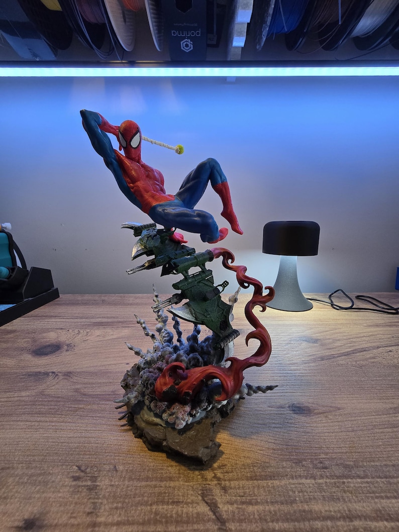 May include: A red and blue Spider-Man action figure is posed in a dynamic action pose. The figure is perched atop a green and gray spaceship-like base with red flames erupting from the base.