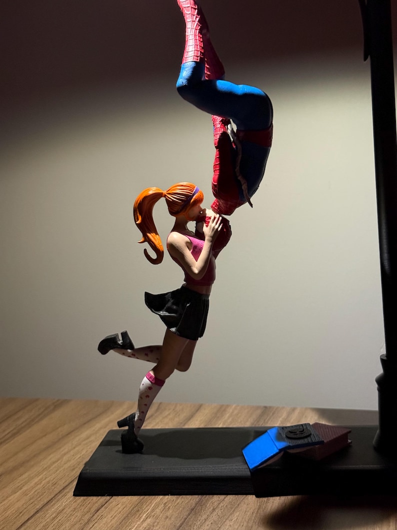 Peut inclure: Figurine repr&eacute;sentant Spider-Man embrassant une femme &agrave; l'envers. La femme porte un haut rose, une jupe noire et des chaussettes blanches &agrave; c&oelig;urs rouges. Spider-Man est dans son costume rouge et bleu classique. La base est noire.