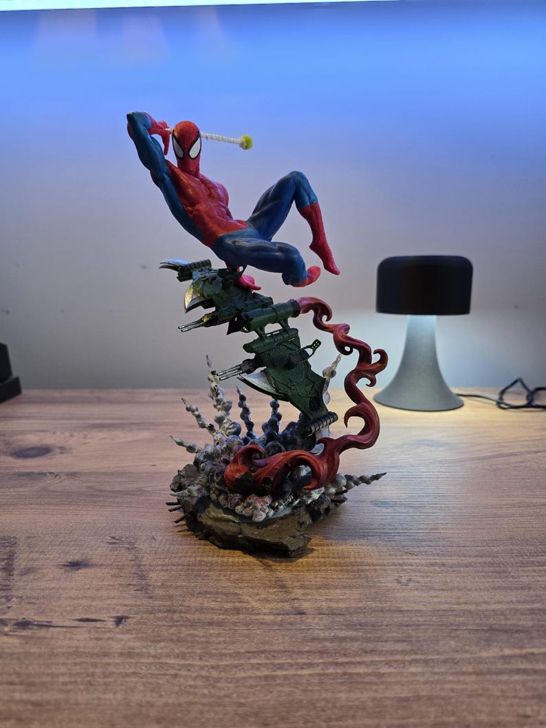 May include: A red and blue Spider-Man action figure is posed in a dynamic action pose, perched atop a green and black spaceship-like base. The base is surrounded by red, black, and white tendrils, creating a dramatic and dynamic scene.